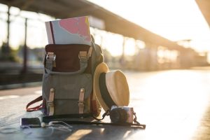 Karta i Ryggsäck, Mobiltelefon med hörlurar och hatt på järnvägsstationen med en traveler.sun set, Resekoncep